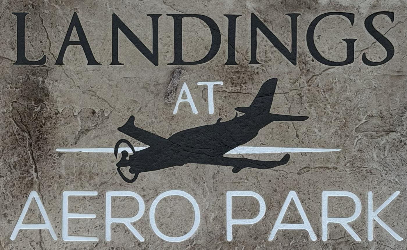 The Landings at Aero Park entrance sign: carved stone lettering with a warbird silhouette between the words Landings and Aero Park